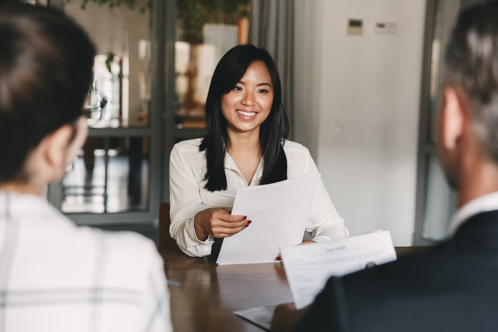 Young woman smiling and holding resume, while interviewing as candidate for a job.